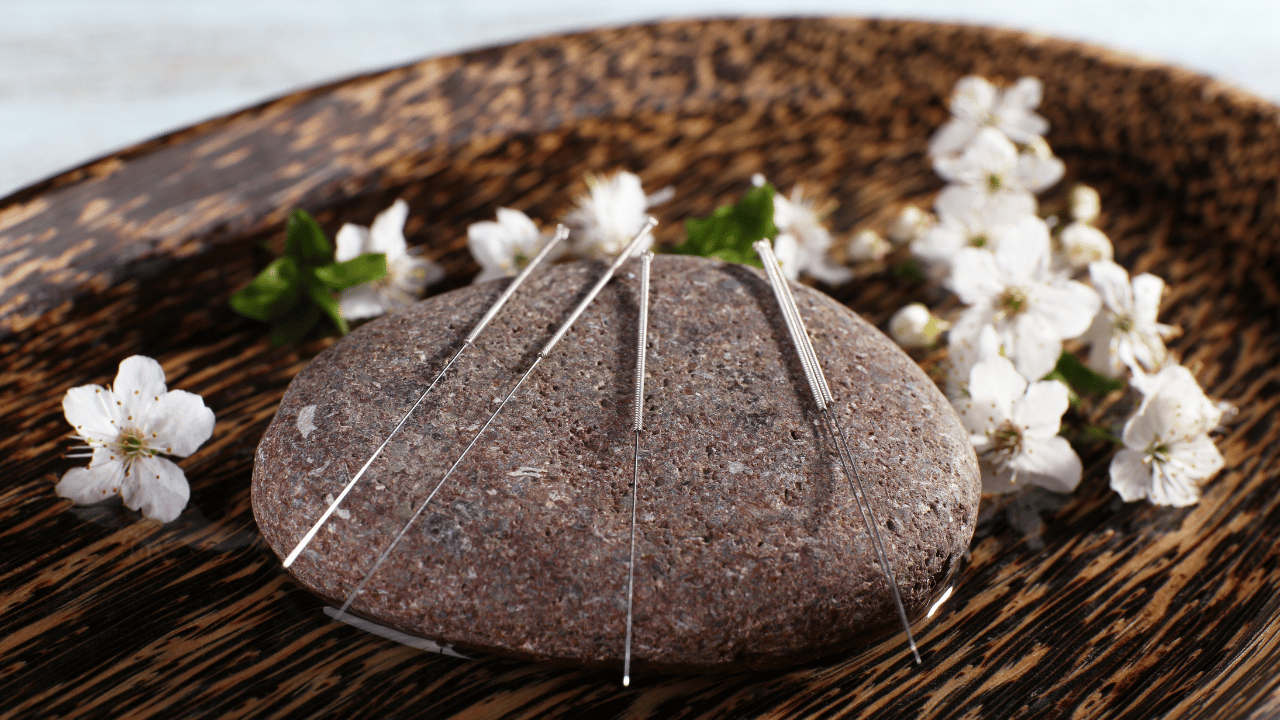 Acupuncture needles and flowers on a wooden plate, offering a holistic therapy for fertility treatments, in Fort Lauderdale, Florida. atma acupuncture