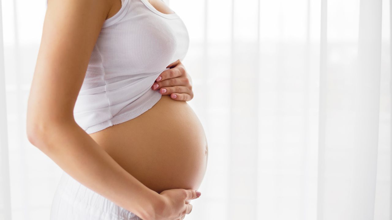 A pregnant woman is gently cupping her stomach in front of a window. atma acupuncture