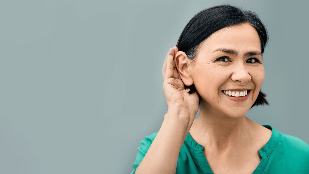 An asian woman is holding her hand up to her ear, possibly engaging in biomagnetic therapy. atma acupuncture